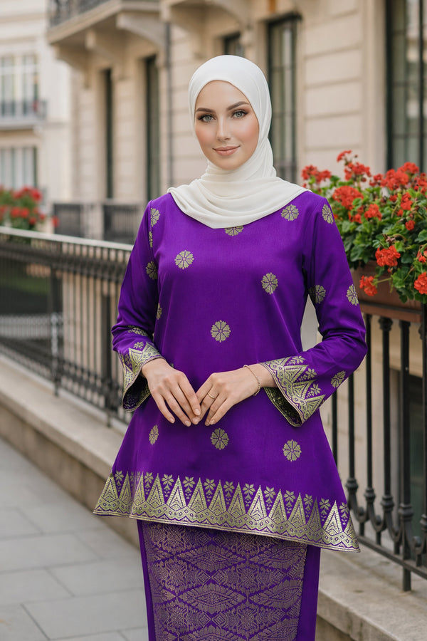 Woman wearing a Kurung Kedah Purple Gold traditional outfit with gold patterns in an urban setting.