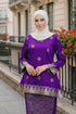 Woman wearing a Kurung Kedah Purple Gold traditional outfit with gold patterns in an urban setting.