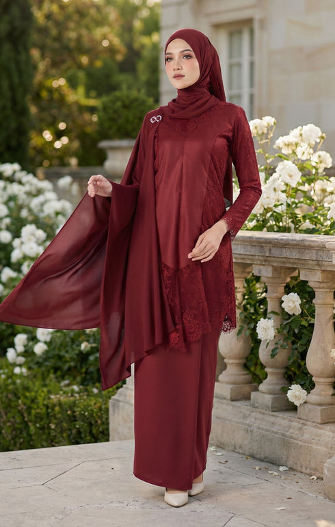 Woman in a Kebaya Moden Maroon close-up outfit standing in a garden with white flowers and stone architecture.