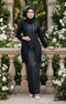 Woman in modern kebaya Kutu Baru Black with Instant Shawl hijab and outfit standing in a garden with white flowers and stone balustrade.