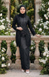 Woman in modern kebaya Kutu Baru Black with Instant Shawl hijab and outfit standing in a garden with white flowers and stone balustrade.