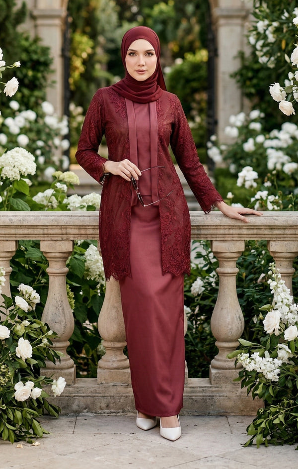 Woman in a kebaya Kutu Baru Maroon outfit standing in a garden with white flowers and stone balustrade.