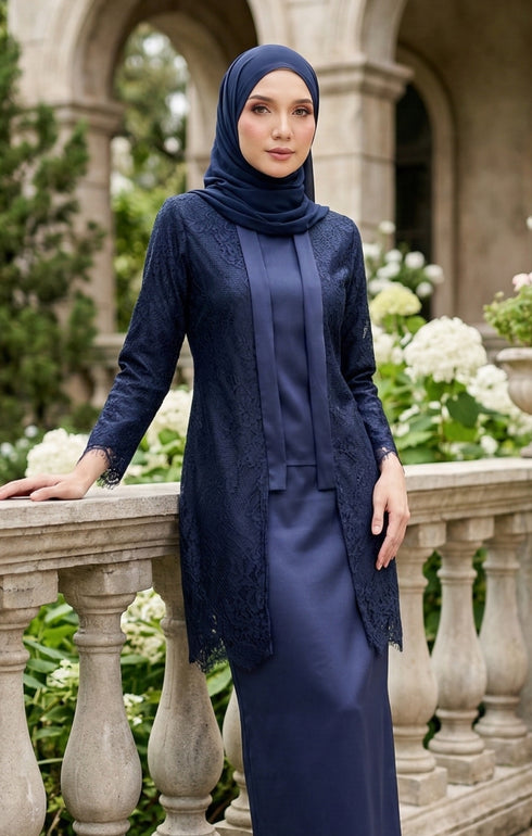 Woman in a baju kebaya Kutu Baru Navy Blue outfit standing in an outdoor setting with floral decorations.