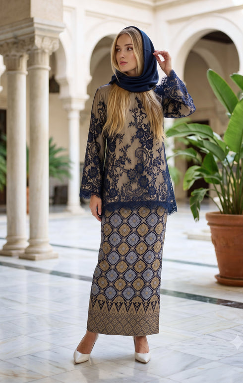 woman posing in Kurung Kedah Lace Songket Blue Black featuring full songket skirt stylingt in an elegant indoor setting with columns and plants.