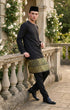 Man in Black Baju Melayu Teluk Belanga traditional attire standing on a stone balcony with floral background