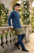 Man in traditional Baju Melayu Teluk Belanga Dark Teal Blue standing on a stone balcony with floral decorations.