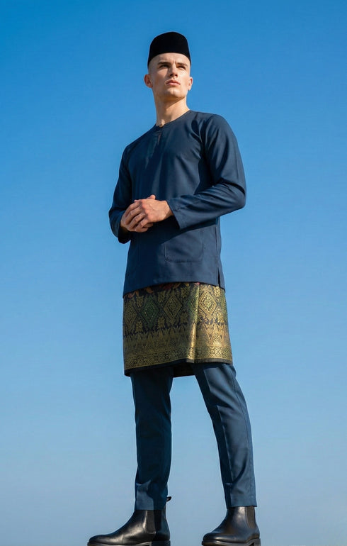 Man wearing a traditional outfit Baju Melayu Teluk Belanga Dark Teal Blue against a clear blue sky.