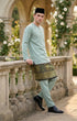 Man in traditional Baju melayu Teluk Belanga attire standing on a stone balcony with floral decorations
