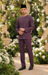 Man in a Baju Melayu Teluk Belanga Dusty Magenta Outfit standing in a garden with white flowers and greenery.