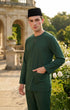 Man wearing a Emerald green traditional baju melayu outfit with a black cap in an outdoor setting.