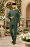 Man in Traditional Baju Melayu Teluk Belanga Emerald Green front view full outfit standing in a decorative outdoor setting with flowers and arches.
