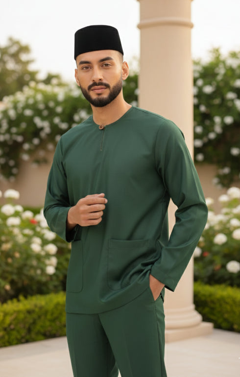 Man wearing a Baju Melayu Teluk Belanga Emerald Green traditional outfit with a black cap in an outdoor setting.