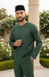 Man wearing a Baju Melayu Teluk Belanga Emerald Green traditional outfit with a black cap in an outdoor setting.