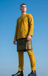 Man wearing Baju Melayu Teluk Belanga Mustard traditional attire with a sampin 3d, against a clear blue sky