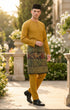 Man wearing Baju Melayu Teluk Belanga Mustard traditional attire with a sampin 3d, standing outdoors.