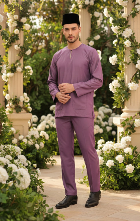 Man wearing a Baju melayu Smokey purple traditional outfit standing in a garden with white flowers and greenery.
