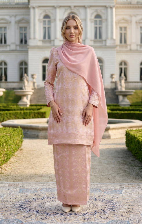 Woman wearing Kurung Moden Dyed Brocade Rose Gold traditional outfit standing in front of a classical building.