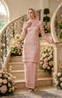 wearing Kurung Moden Dyed Brocade Rose Gold standing on a decorated staircase with floral arrangements.