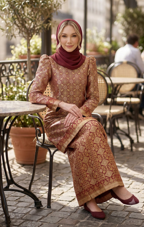 model styling Kurung Moden Dyed Brocade Burgundy sitting outdoors at a cafe.