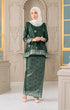 Woman wearing a Kurung Kedah Dark Emerald Green Silver traditional outfit with a matching Shawl Hijab in an elegant interior setting.