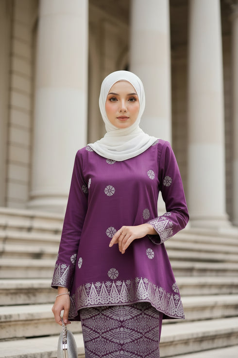Woman wearing a Kurung Kedah Magenta Silver traditional outfit with white patterns in an elegant interior setting.