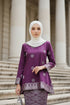 Woman wearing a Kurung Kedah Magenta Silver traditional outfit with white patterns in an elegant interior setting.