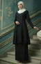 Woman in a Kebarung Klasik Plain Black outfit with a plain white hijab standing on a staircase with decorative walls.