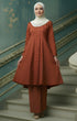 Woman in a Kebarung Klasik Plain Brick Orange front view outfit standing on a staircase with decorative walls.