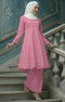 Woman in a Kebarung Klasik Plain Pink dress standing on a staircase with a decorative blue wall in the background