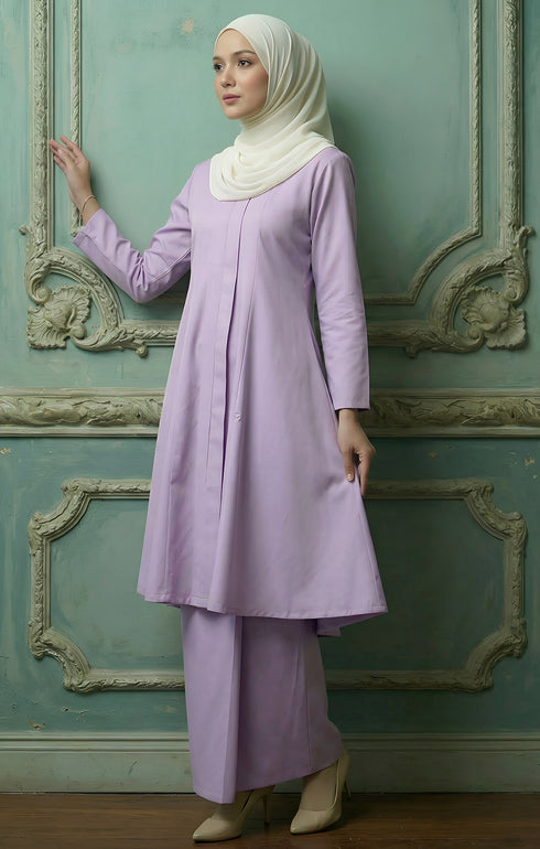 Kebarung Klasik Plain Dusty Purple outfit with a white hijab against a decorative green wall.