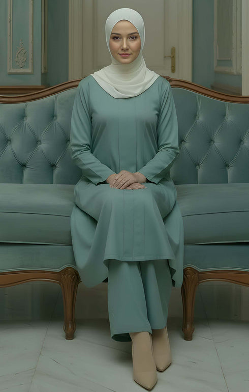 Woman Kebarung Klasik Plain Sage Green outfit sitting on a light blue couch in a decorated room.