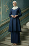 Woman in a Kebarung Klasik Plain Navy Blue full outfit view with lipat depan kain detail standing on a staircase with decorative walls.