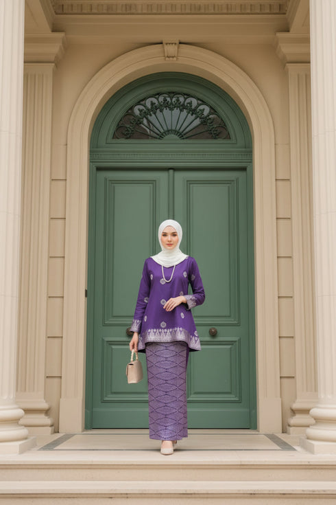 Woman in a Kurung Kedah Magenta Silver outfit standing in front of a green door.