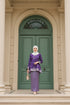 Woman in a Kurung Kedah Magenta Silver outfit standing in front of a green door.