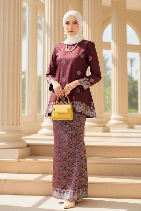 Woman wearing a Kurung Kedah Dark Maroon Silver traditional outfit in an elegant interior setting.