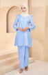 A woman wearing a baby blue traditional Kurung Riau Plain outfit with a V-neck top and long straight sleeves, standing in a studio setting.