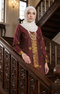 Woman in a Seroja Kebaya Dark Maroon Gold traditional outfit standing on a staircase.
