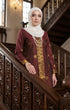 Woman in a Seroja Kebaya Dark Maroon Gold traditional outfit standing on a staircase.