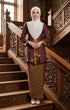 Woman in traditional attire Seroja Kebaya Dark Maroon Gold standing on a wooden staircase with intricate carvings.