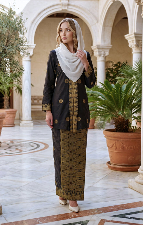 woman wearing Kebaya Kurung Moden Songket Black Gold front view standing in a decorative outdoor setting.