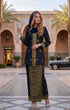 Woman in traditional Kebaya Songket Black Gold outfit standing in a courtyard with architectural elements and a car in the background.