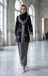 Woman in a Kebaya Kurung Moden Songket Black Silver standing in a grand hall with high ceilings and large windows.