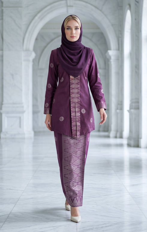 Woman wearing a traditional outfit baju kebaya songket bunga tabur magenta silver with a matching hijab in a marble hallway.