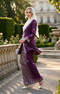 woman wearing baju kebaya songket bunga tabur magenta silver traditional outfit standing in a garden with classical architecture.