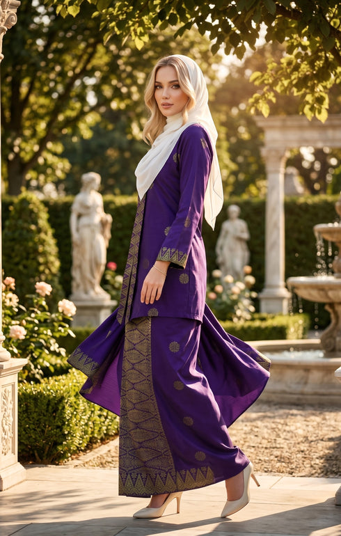 Woman in a Baju kebaya songket bunga tabur purple gold outfit standing in a garden with statues and flowers.