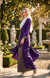 Woman in a Baju kebaya songket bunga tabur purple gold outfit standing in a garden with statues and flowers.