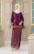 Woman wearing a Kurung Kedah Magenta Gold traditional outfit with gold accents against an ornate wall.