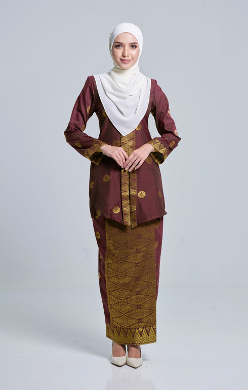A woman wearing a Seroja Kebaya Dark Maroon Gold traditional dress with long straight sleeves, a V-neck collar, and a back zip. The dress features a songket pattern with a border design.