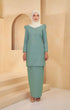 A woman Kurung Moden Plain Dusty Green, slim-fit, cotton plain kurung with a round neck and long straight sleeves, standing against a beige background.