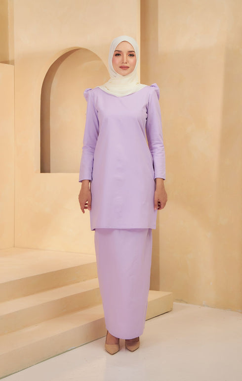 A woman wearing a Kurung Moden Plain Dusty Purple, solid-patterned, long-sleeved traditional dress with a round neckline, standing against a neutral background.